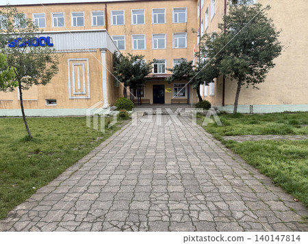 a brick walkway leads to a school building with a sign a brick walkway leads to a school building with a sign 140147814