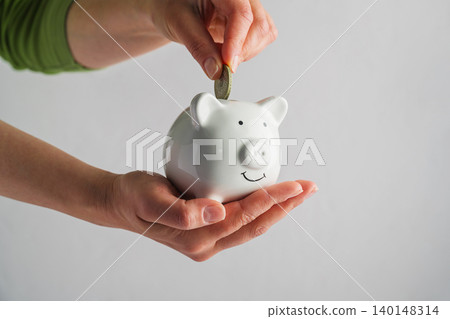 Person putting coin into piggy bank, savings personal finance budgeting and financial growth concept Person putting coin into piggy bank, savings personal finance budgeting and financial growth concept 140148314