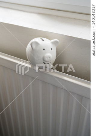 Piggy bank on home radiator, household energy savings heating costs and utility budget concept Piggy bank on home radiator, household energy savings heating costs and utility budget concept 140148317