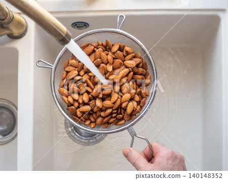 Man washes almonds in a metal colander Man washes almonds in a metal colander 140148352