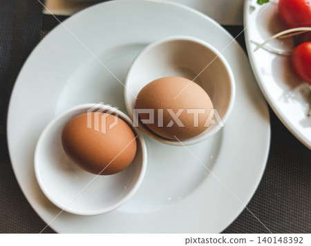 Two brown eggs in white cups on a plate Two brown eggs in white cups on a plate 140148392