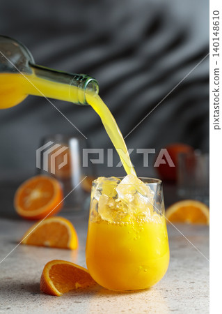 Orange juice is poured into a glass with ice. Orange juice is poured into a glass with ice. 140148610