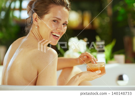 Mid-Adult Woman Smiling in Bathtub with Scrub Mid-Adult Woman Smiling in Bathtub with Scrub 140148733