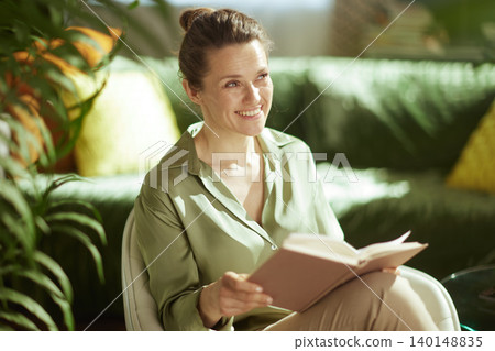 Woman Smiling and Reading Book in Sunlit Living Room 140148835