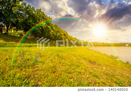 sunset over longest linden alley in europe on the Uzh river embankment. lime trees in summer. travel destination of transcarpathia. uzhhorod street cityscape beauty. weather with rainbow sunset over longest linden alley in europe on the Uzh river embankment. lime trees in summer. travel destination of transcarpathia. uzhhorod street cityscape beauty. weather with rainbow 140148920