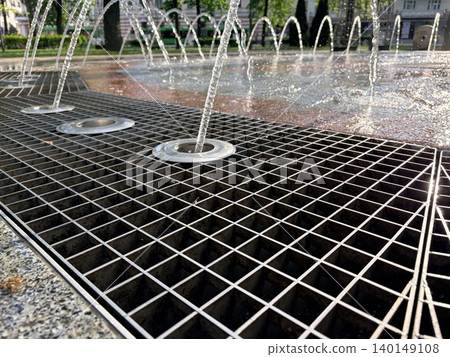 a close-up, low-angle view of a modern urban ground fountain or splash pad on a sunny day. a close-up, low-angle view of a modern urban ground fountain or splash pad on a sunny day. 140149108