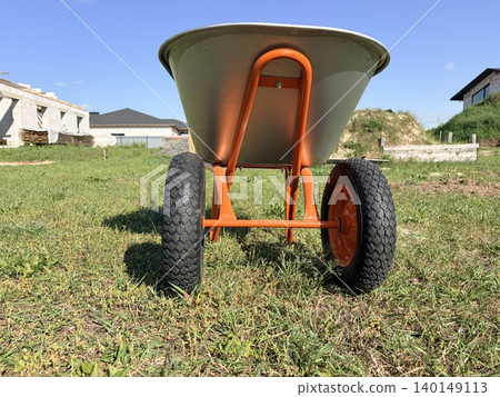 a sturdy, two-wheeled wheelbarrow positioned centrally on a patch of green grass a sturdy, two-wheeled wheelbarrow positioned centrally on a patch of green grass 140149113