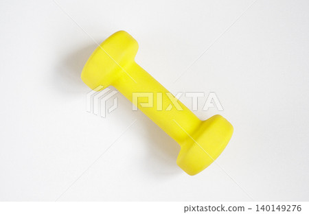 Small yellow dumbbell on a light gray background, preparing for a home workout. Kettlebells, angle, fitness, minimalism, sunny, floor, reusable. Small yellow dumbbell on a light gray background, preparing for a home workout. Kettlebells, angle, fitness, minimalism, sunny, floor, reusable. 140149276