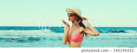 Summer vacation, beautiful young woman blowing kiss in bikini swimsuit, tourist hat on beach on sea Summer vacation, beautiful young woman blowing kiss in bikini swimsuit, tourist hat on beach on sea 140149332