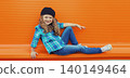 Happy cheerful kid girl dancer with curly hair, joyful child dancing in the city on orange wall 140149464