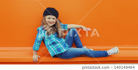 Happy cheerful kid girl dancer with curly hair, joyful child dancing in the city on orange wall Happy cheerful kid girl dancer with curly hair, joyful child dancing in the city on orange wall 140149464