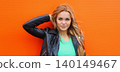 Portrait beautiful young blonde woman posing in black leather jacket on colorful orange background 140149467