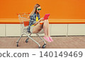 Modern young woman using digital tablet computer sitting in shopping trolley cart on city street 140149469