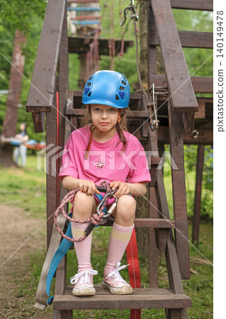 A sad child in a helmet in protective gear with a belt and a carbine is trying to overcome the fear of passing the track in an active recreation park A sad child in a helmet in protective gear with a belt and a carbine is trying to overcome the fear of passing the track in an active recreation park 140149478