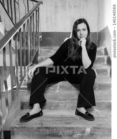 woman sits on a concrete staircase in the entrance, propping up her chin with her hand woman sits on a concrete staircase in the entrance, propping up her chin with her hand 140149569