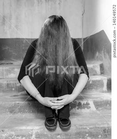 woman sits on the steps, completely covering her face with long hair woman sits on the steps, completely covering her face with long hair 140149572
