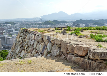 米子城城堡塔基上保留著歷史悠久的石牆和長凳,米子市和周圍的山脈在背景中綿延展開(鳥取縣米子市)。 米子城城堡塔基上保留著歷史悠久的石牆和長凳,米子市和周圍的山脈在背景中綿延展開(鳥取縣米子市)。 140149650