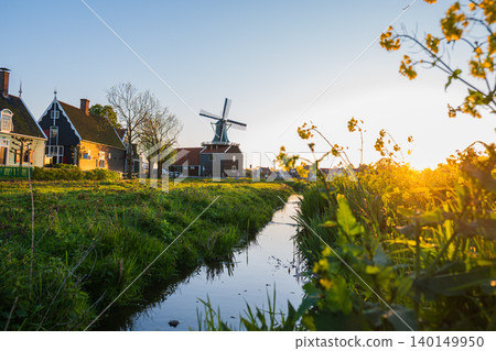 Beautiful Dutch countryside landscape with traditional windmill, canal, green fields and historic houses illuminated by warm golden hour sunlight in the Netherlands. Beautiful Dutch countryside landscape with traditional windmill, canal, green fields and historic houses illuminated by warm golden hour sunlight in the Netherlands. 140149950