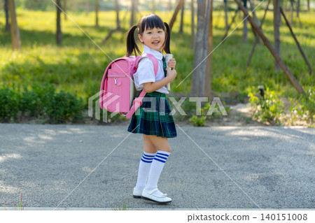 Asian primary school students walk home from school with their backpacks and books. 140151008