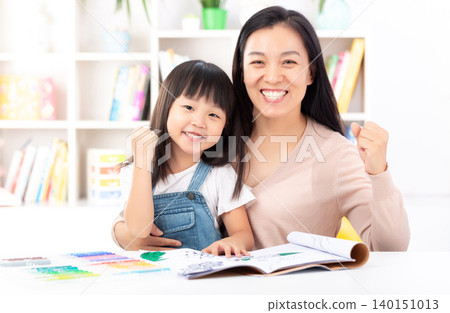 A proud mother and her young daughter sitting together at a desk and cheering with raised fists to show success and confidence. A proud mother and her young daughter sitting together at a desk and cheering with raised fists to show success and confidence. 140151013