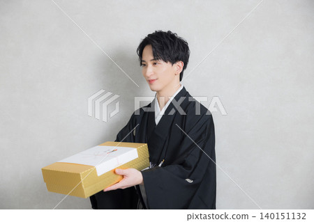 一位穿著和服的年輕男子手捧祝賀禮物。 一位穿著和服的年輕男子手捧祝賀禮物。 140151132