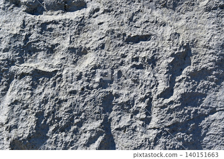 A concrete wall texture with a rough, uneven surface like rock; a background material with a rough texture and shadows. A concrete wall texture with a rough, uneven surface like rock; a background material with a rough texture and shadows. 140151663