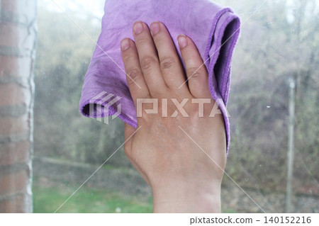 The girl wipes the window with a napkin. Close-up The girl wipes the window with a napkin. Close-up 140152216