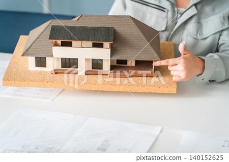 A woman in work clothes, working in the construction or building industry, uses a model house to conduct business negotiations, explanations, and presentations. A woman in work clothes, working in the construction or building industry, uses a model house to conduct business negotiations, explanations, and presentations. 140152625