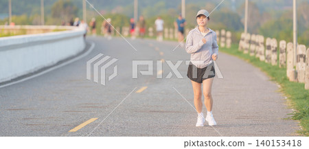 Active young Asian woman jogging and running in the public park at morning. female athlete in sportswear exercising for healthy lifestyle and fitness workout outdoors. Wellness and sport concepts 140153418