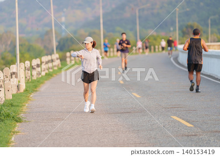 Active Asian woman checking her smartwatch while jogging in the park. Female runner tracking heart rate and progress during outdoor fitness workout. Wearable technology and healthy lifestyle concept Active Asian woman checking her smartwatch while jogging in the park. Female runner tracking heart rate and progress during outdoor fitness workout. Wearable technology and healthy lifestyle concept 140153419