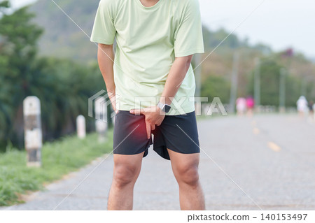 Young adult male runner suffering from acute groin pull and muscle pain during running workout. Man holding his inner thigh due to sports injury and strain. Medical and healthcare concept Young adult male runner suffering from acute groin pull and muscle pain during running workout. Man holding his inner thigh due to sports injury and strain. Medical and healthcare concept 140153497