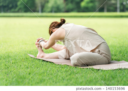 A woman stretches, warms up, and bends forward on the grass in a park. A woman stretches, warms up, and bends forward on the grass in a park. 140153696