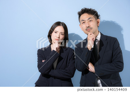 一位商人和一位女士穿著西裝,雙手托著下巴,直視鏡頭,思考著商業策略,並努力打造 B2B 形象。 一位商人和一位女士穿著西裝,雙手托著下巴,直視鏡頭,思考著商業策略,並努力打造 B2B 形象。 140154409