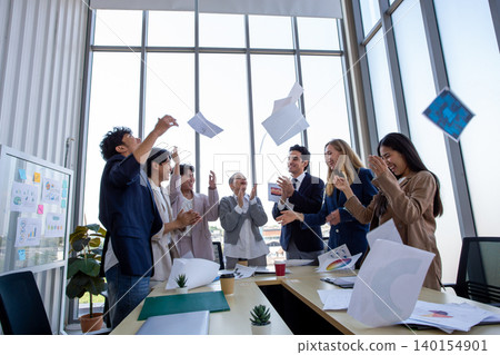 Happy business team celebrating success in office by throwing documents in the air. Corporate achievement, teamwork, motivation, workplace happiness, and startup success concept. Happy business team celebrating success in office by throwing documents in the air. Corporate achievement, teamwork, motivation, workplace happiness, and startup success concept. 140154901
