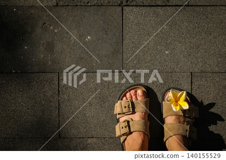 Someone stands on stone tiles in Bali with sandals and a flower Someone stands on stone tiles in Bali with sandals and a flower 140155529