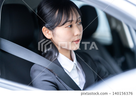 一位身穿西裝的年輕女子正在開車。出差、拜訪客戶、開車。 140156376