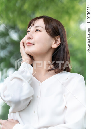 A smiling woman caring for her skin outdoors. Anti-aging. Fresh greenery. Advertising material. 140156384