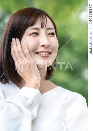 一位微笑的女士在戶外護理肌膚。抗衰老。清新綠植。廣告素材。 一位微笑的女士在戶外護理肌膚。抗衰老。清新綠植。廣告素材。 140156387