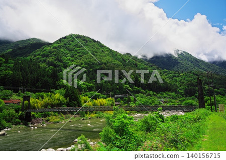 The Morohara Bridge, a suspension bridge spanning the Kiso River surrounded by fresh greenery, and a train. The Morohara Bridge, a suspension bridge spanning the Kiso River surrounded by fresh greenery, and a train. 140156715