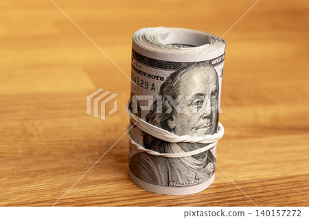Roll of US hundred dollar bills with rubber band on wooden background. Roll of US hundred dollar bills with rubber band on wooden background. 140157272
