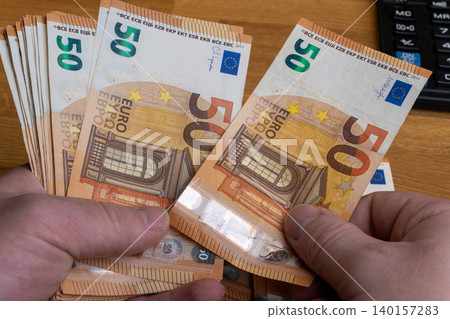 Hands counting 50 Euro banknotes stack on office desk close up Hands counting 50 Euro banknotes stack on office desk close up 140157283