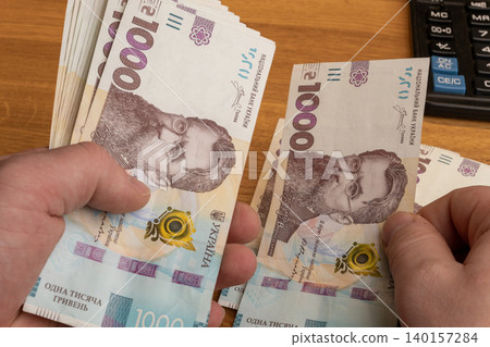Hands counting 1000 Ukrainian hryvnia banknotes on office desk close up Hands counting 1000 Ukrainian hryvnia banknotes on office desk close up 140157284