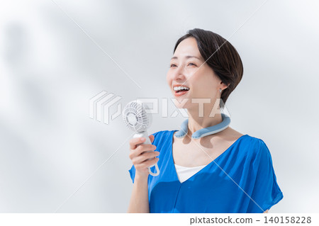 A woman using an ice ring and a handheld fan in the summer. A woman using an ice ring and a handheld fan in the summer. 140158228