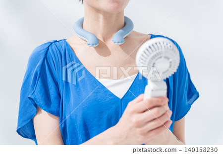 A woman using an ice ring and a handheld fan in the summer. A woman using an ice ring and a handheld fan in the summer. 140158230