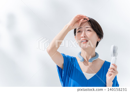 A woman using an ice ring and a handheld fan in the summer. A woman using an ice ring and a handheld fan in the summer. 140158231