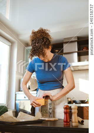 Woman is grating cheese using a metal hand grater Woman is grating cheese using a metal hand grater 140158737