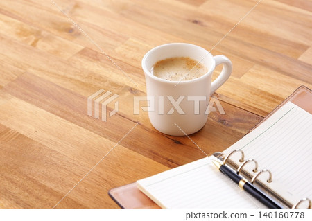 一張圖片:某人在辦公桌前使用筆記本工作,同時喝著加大量牛奶的咖啡或拿鐵咖啡。 一張圖片:某人在辦公桌前使用筆記本工作,同時喝著加大量牛奶的咖啡或拿鐵咖啡。 140160778
