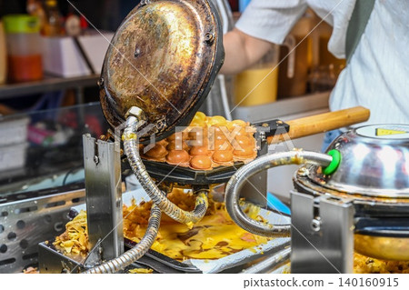Baking traditional crispy bubble waffle in professional egg waffle maker machine at Temple Street Night Market street food stall in Hong Kong Baking traditional crispy bubble waffle in professional egg waffle maker machine at Temple Street Night Market street food stall in Hong Kong 140160915