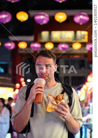 Handsome 30 years old Russian man tourist eating traditional bubble waffle and drinking iced lemon tea at Temple Street Night Market in Hong Kong Handsome 30 years old Russian man tourist eating traditional bubble waffle and drinking iced lemon tea at Temple Street Night Market in Hong Kong 140160917