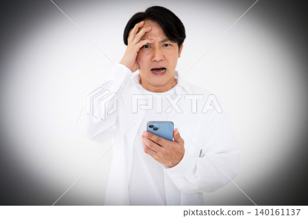 A casually dressed middle-aged man is shocked when he looks at his smartphone. A casually dressed middle-aged man is shocked when he looks at his smartphone. 140161137